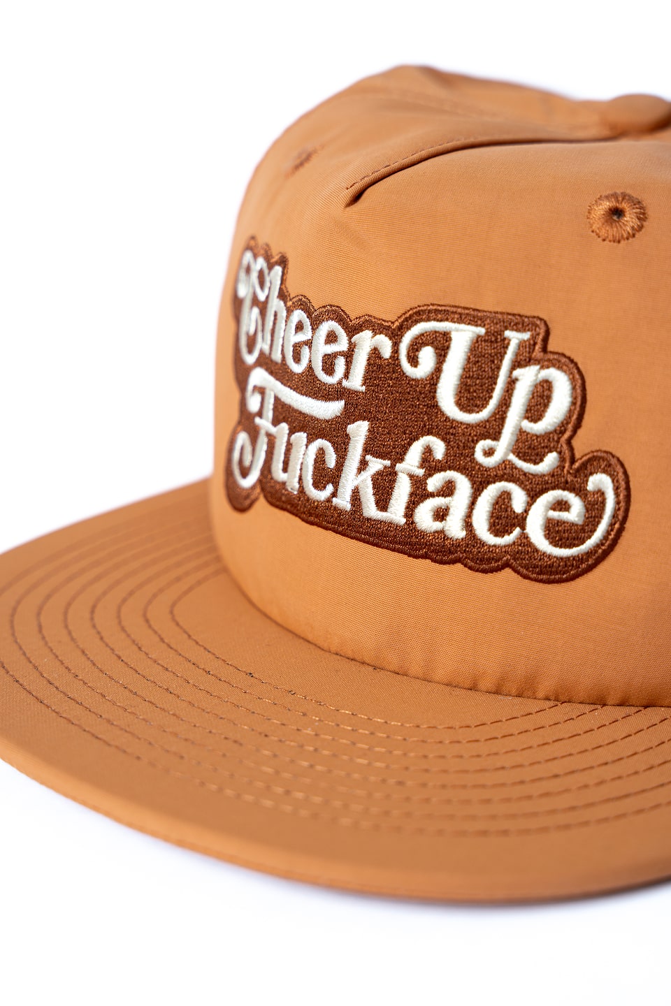 Caramel snapback cap with cream text 'CheerUp Fuckface' embroidered on the front, side angle