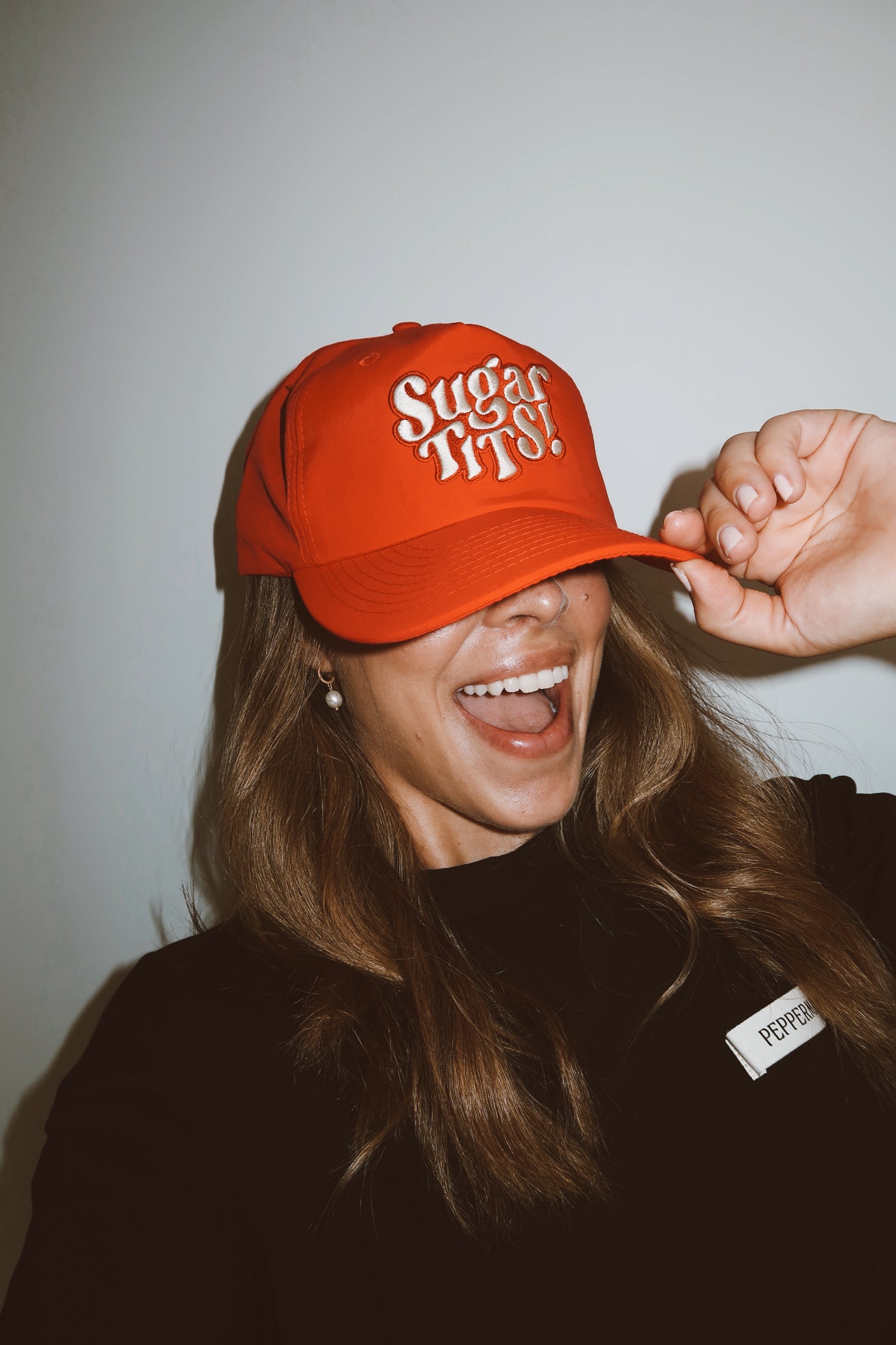 lady wearing an red cap with text, laughing against a plain background