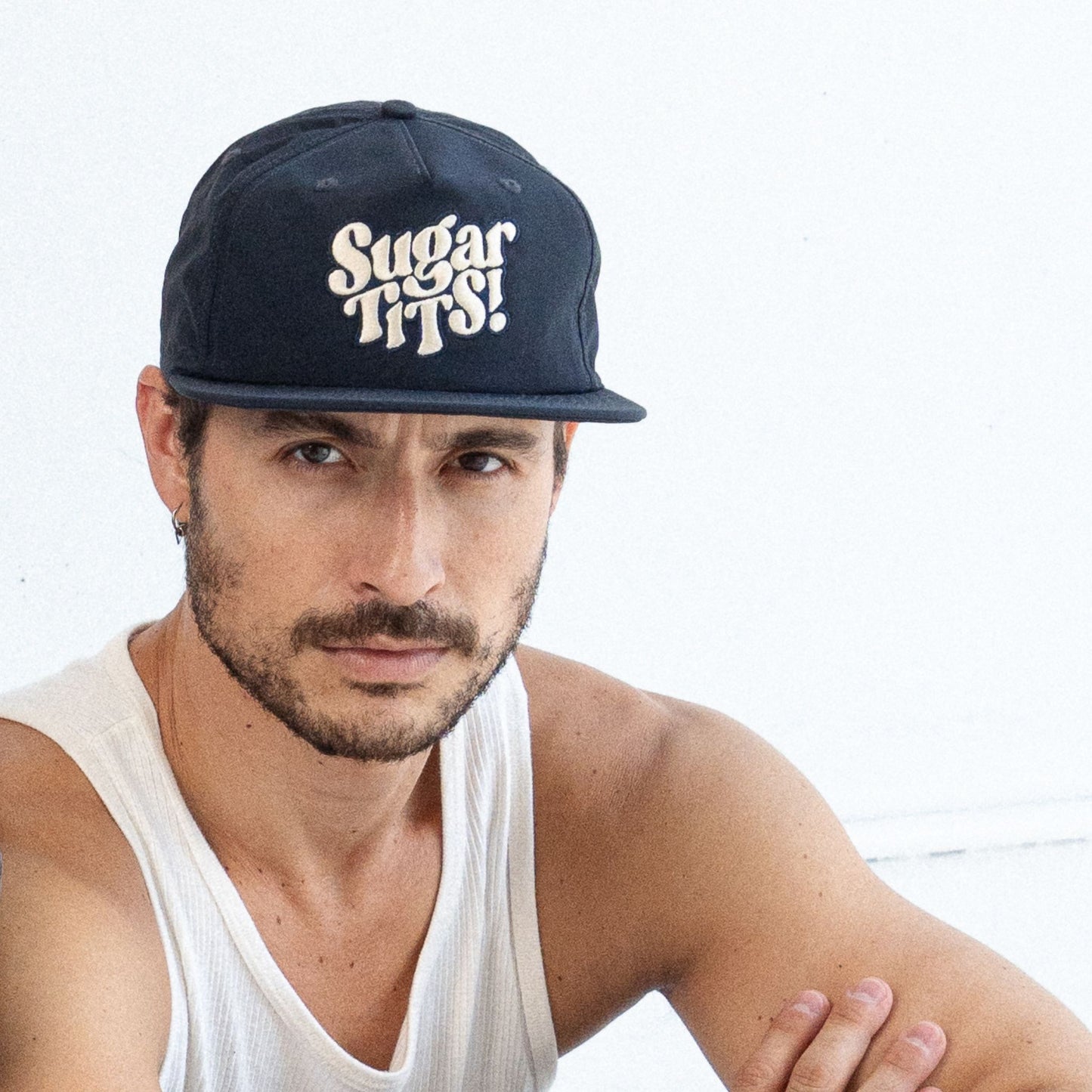 Man wearing a navy blue cap with 'Sugar Tits!' text on a white background